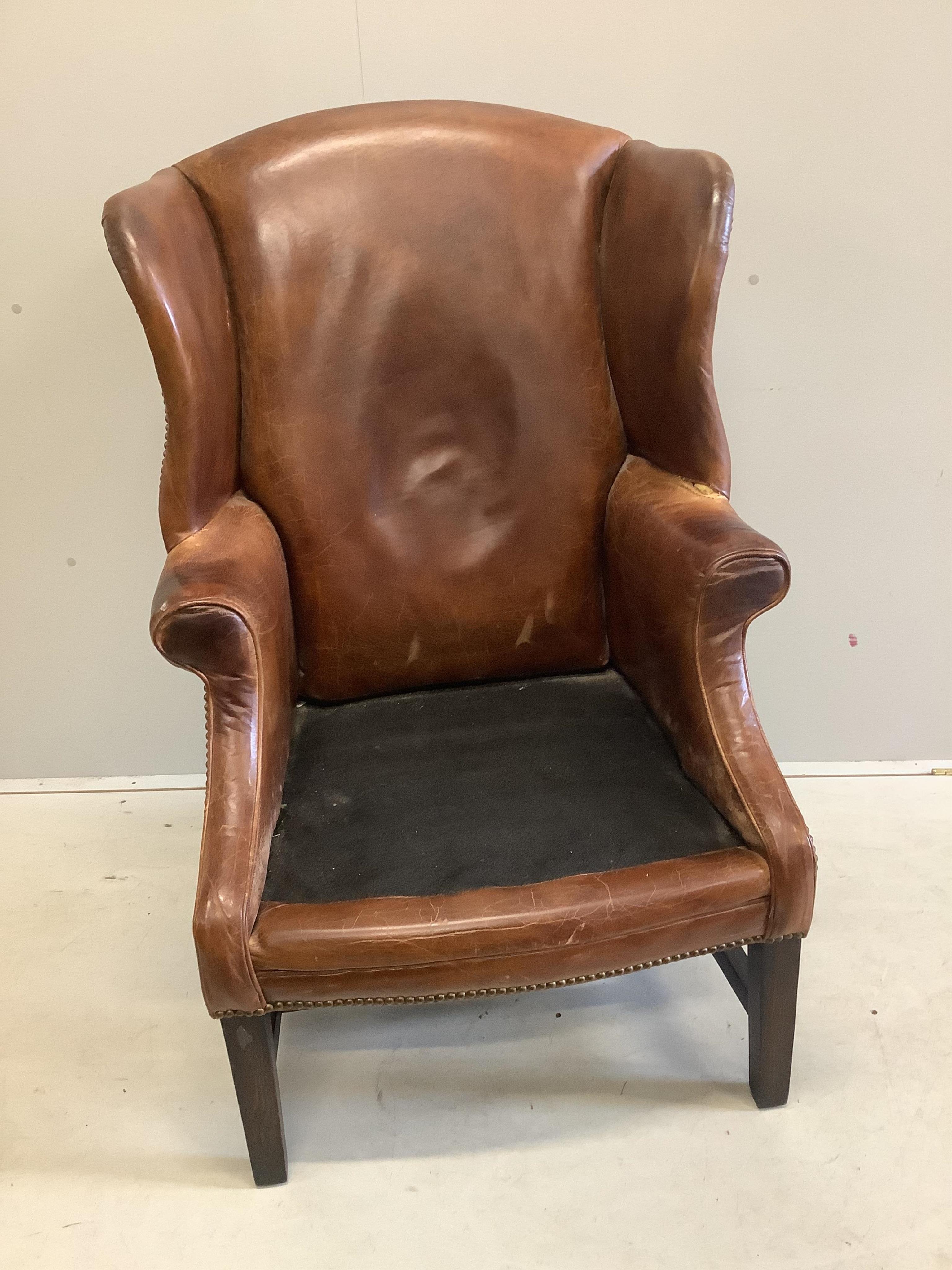 A George III style oak and tan leather wing back armchair, width 76cm, depth 70cm, height 112cm. Condition - poor to fair